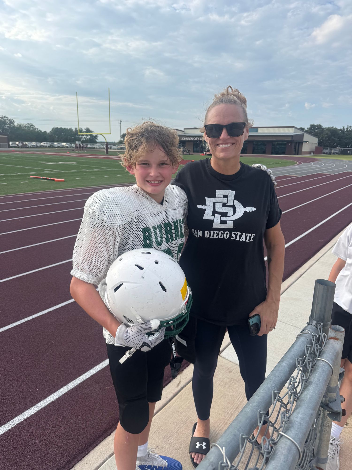 Amber and her oldest son at the field before his first football game, him in his jersey holding his helmet