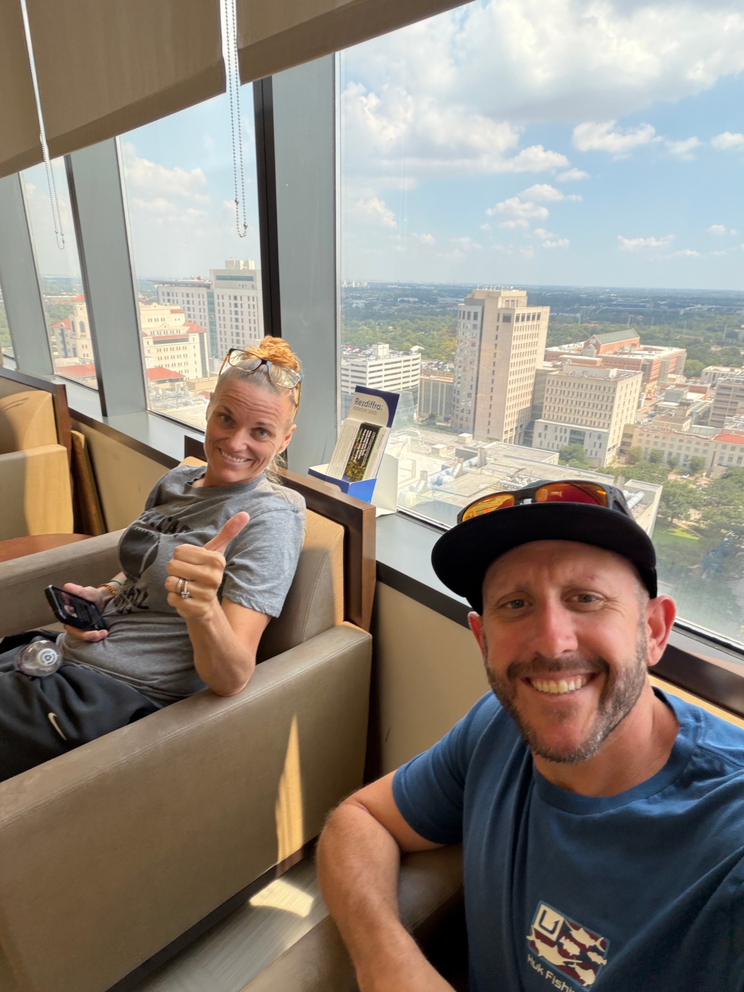 Amber giving a thumbs up in a Houston Methodist waiting room high above the medical center, with Ryan in the foreground
